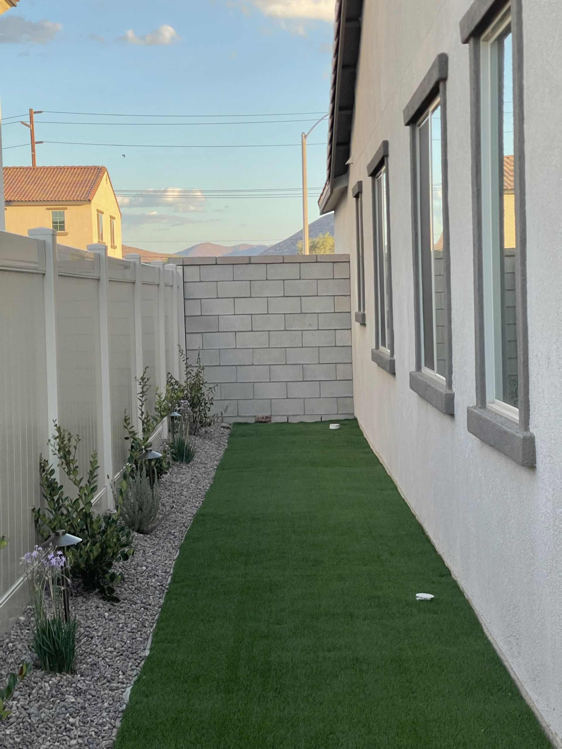 A narrow backyard with artificial turf, white fence, and house.