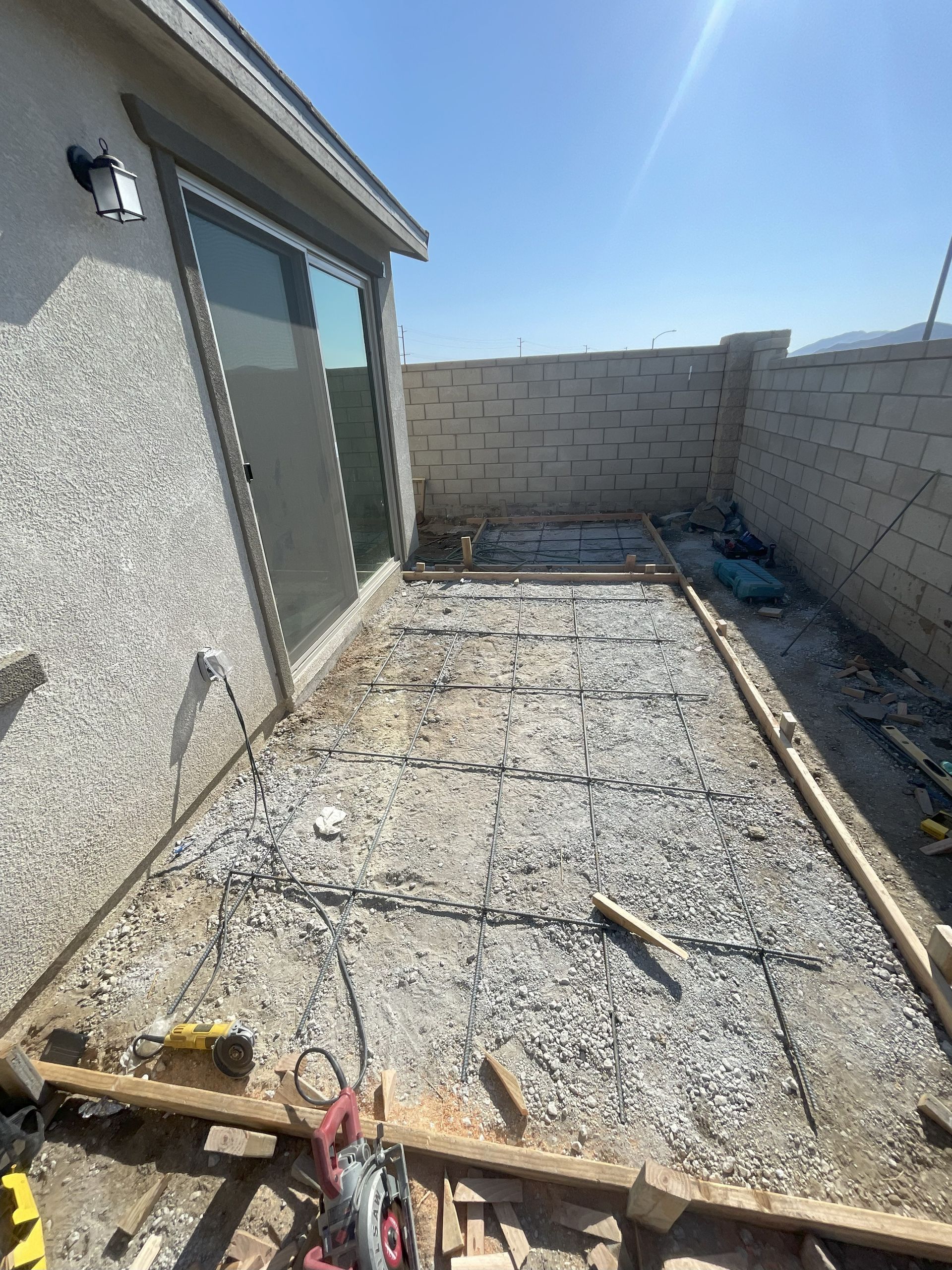 Construction site in a backyard. Gravel base within wooden frame, near a sliding glass door and brick wall.