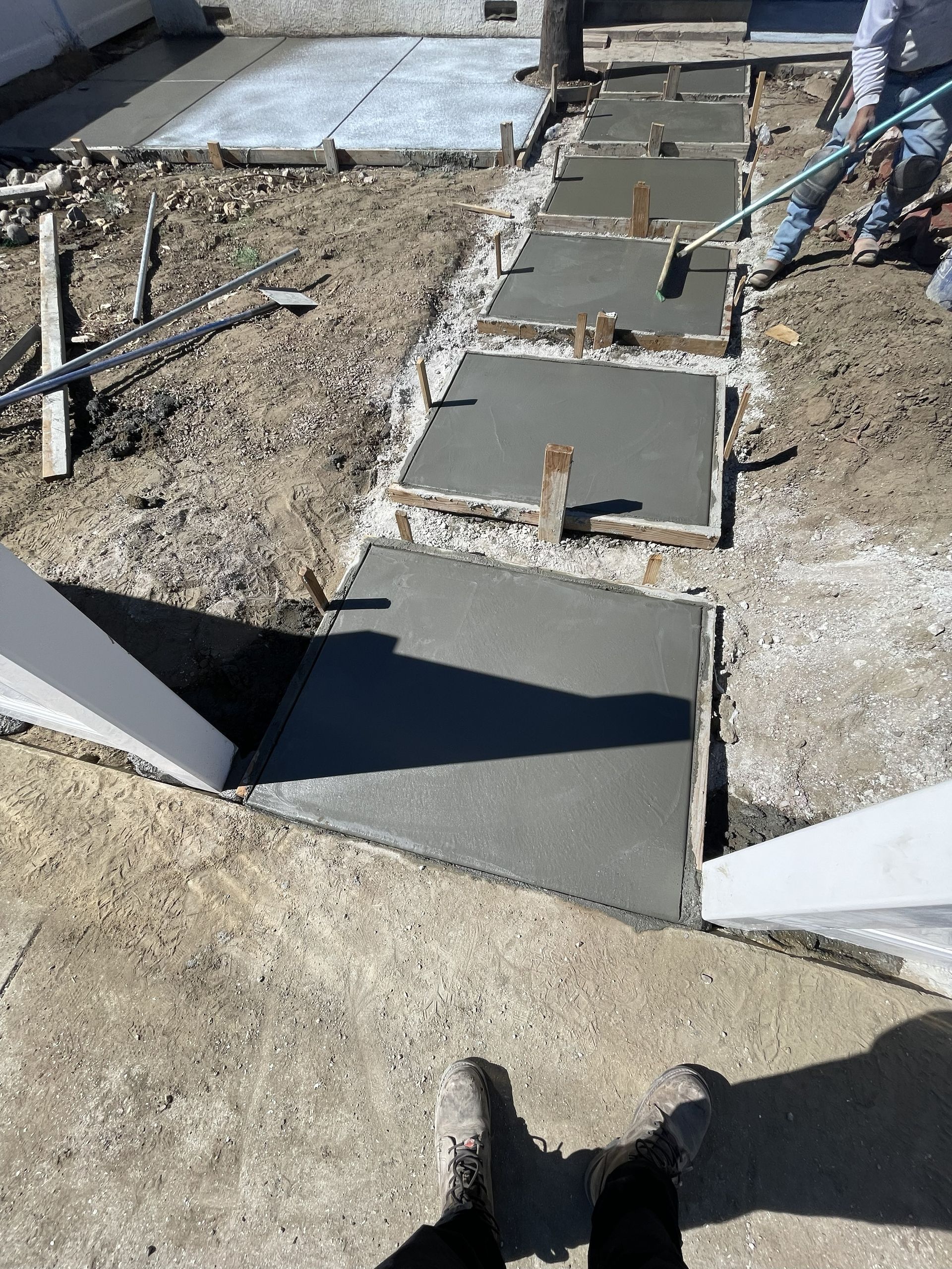 Concrete pathway being poured between wooden forms, outdoors.