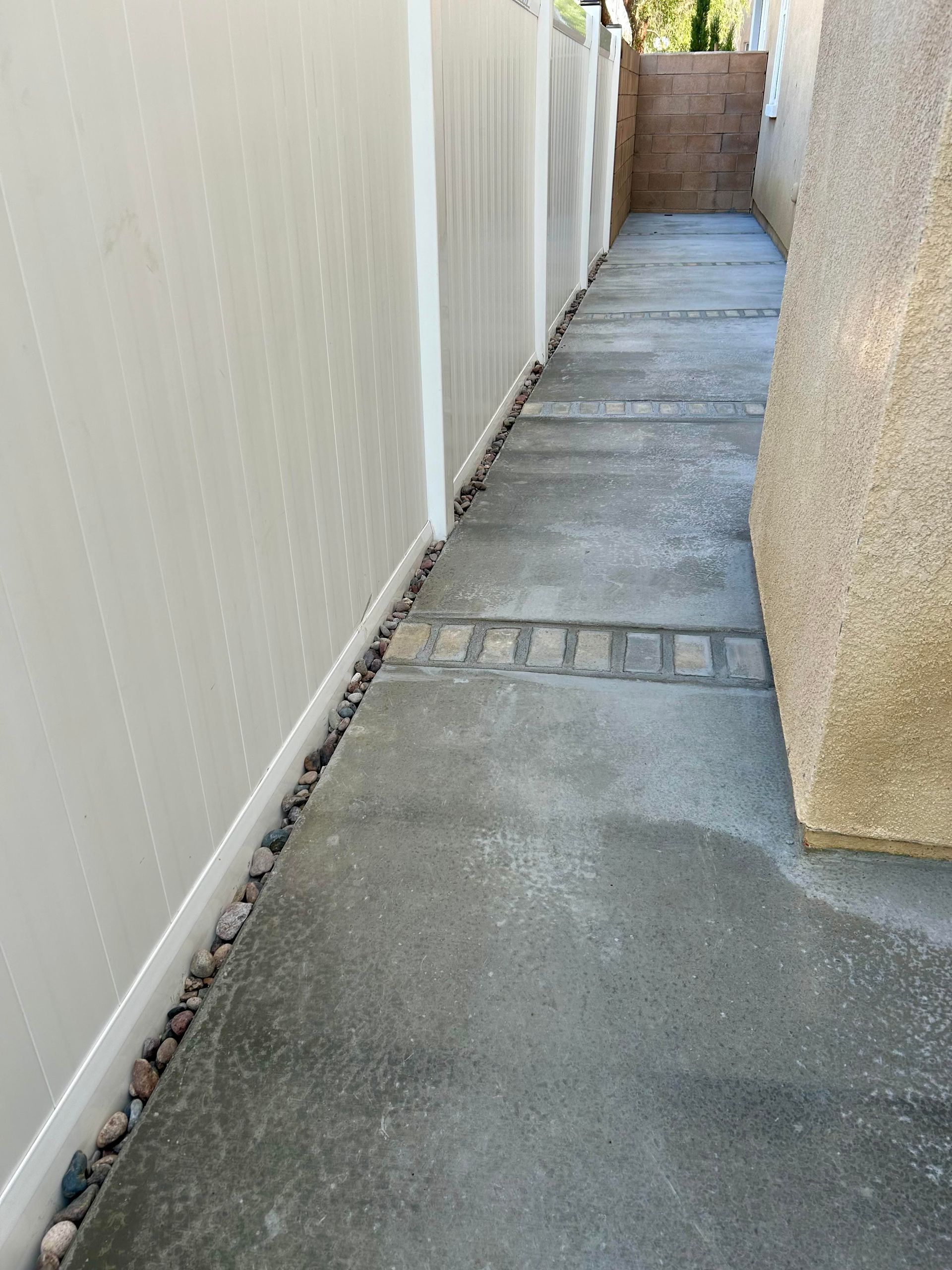 A concrete walkway between two buildings with a white fence.