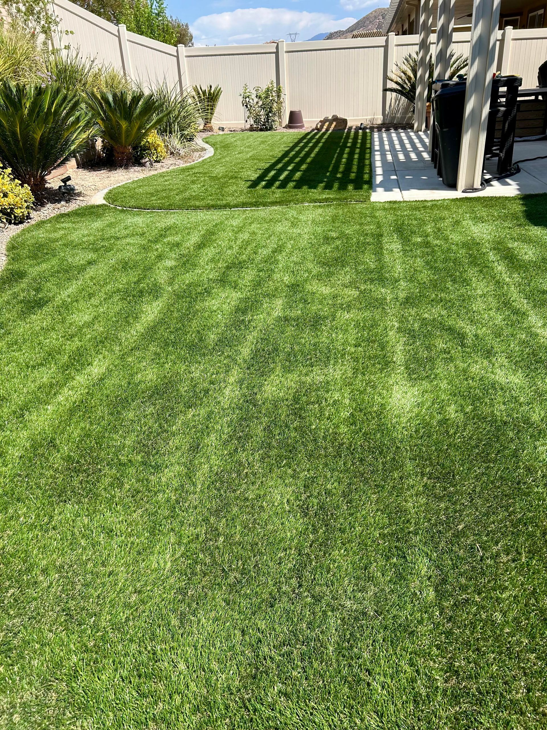 Green backyard with artificial turf, plants, and a fence.