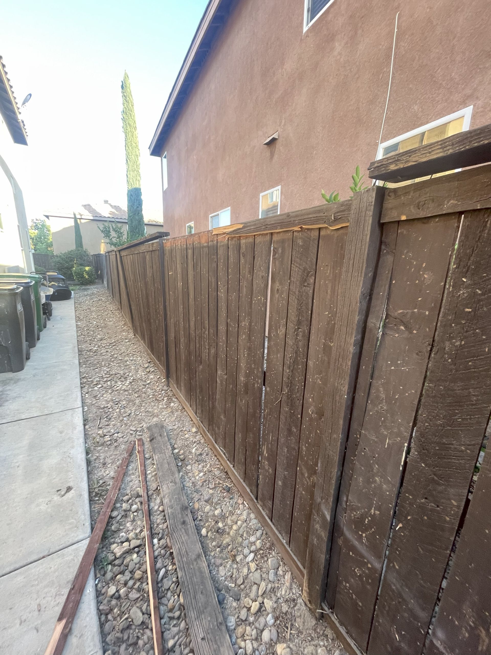 Wooden fence alongside a gravel path and a brown building.