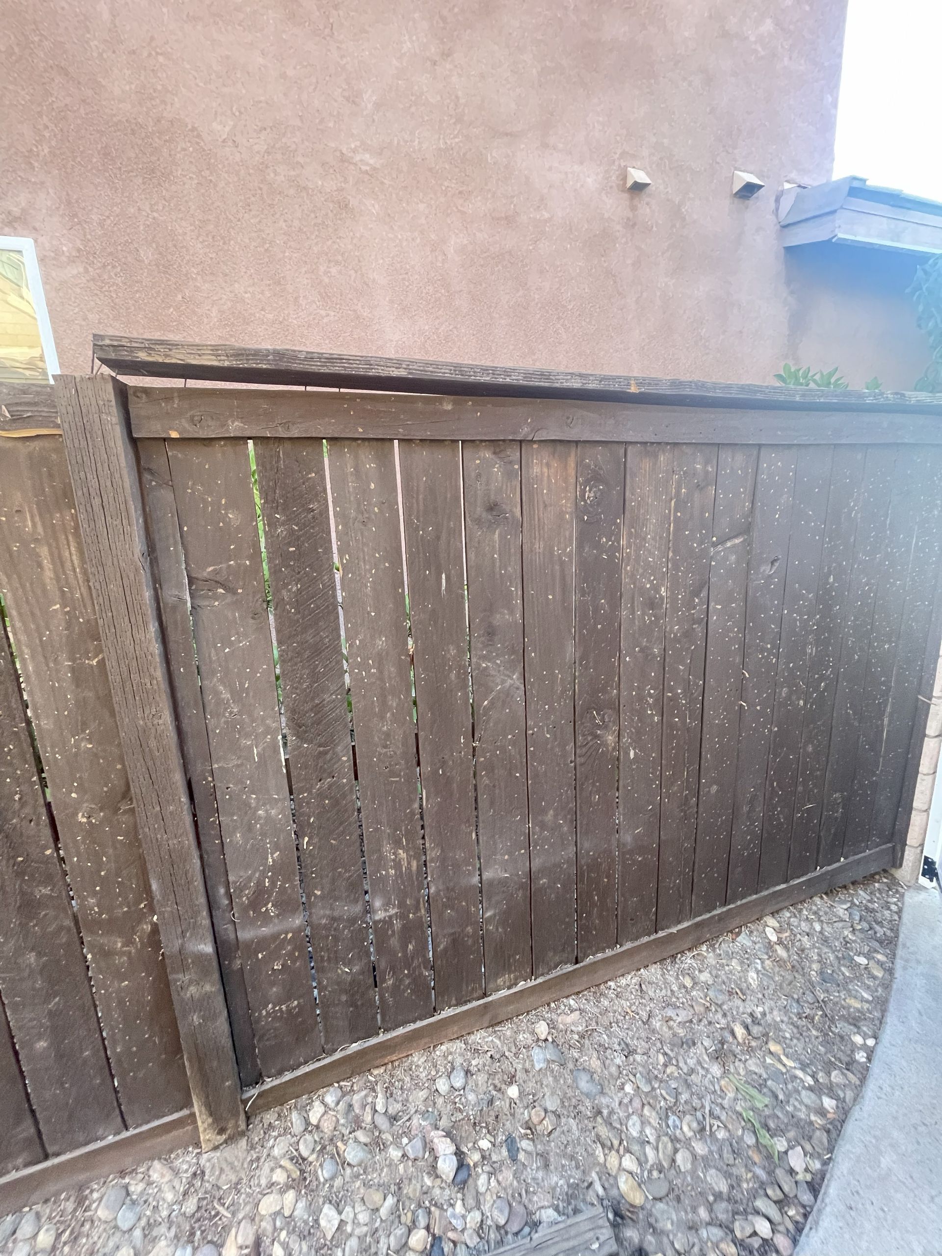 Wooden fence with white spots against a stucco wall, set on gravel.