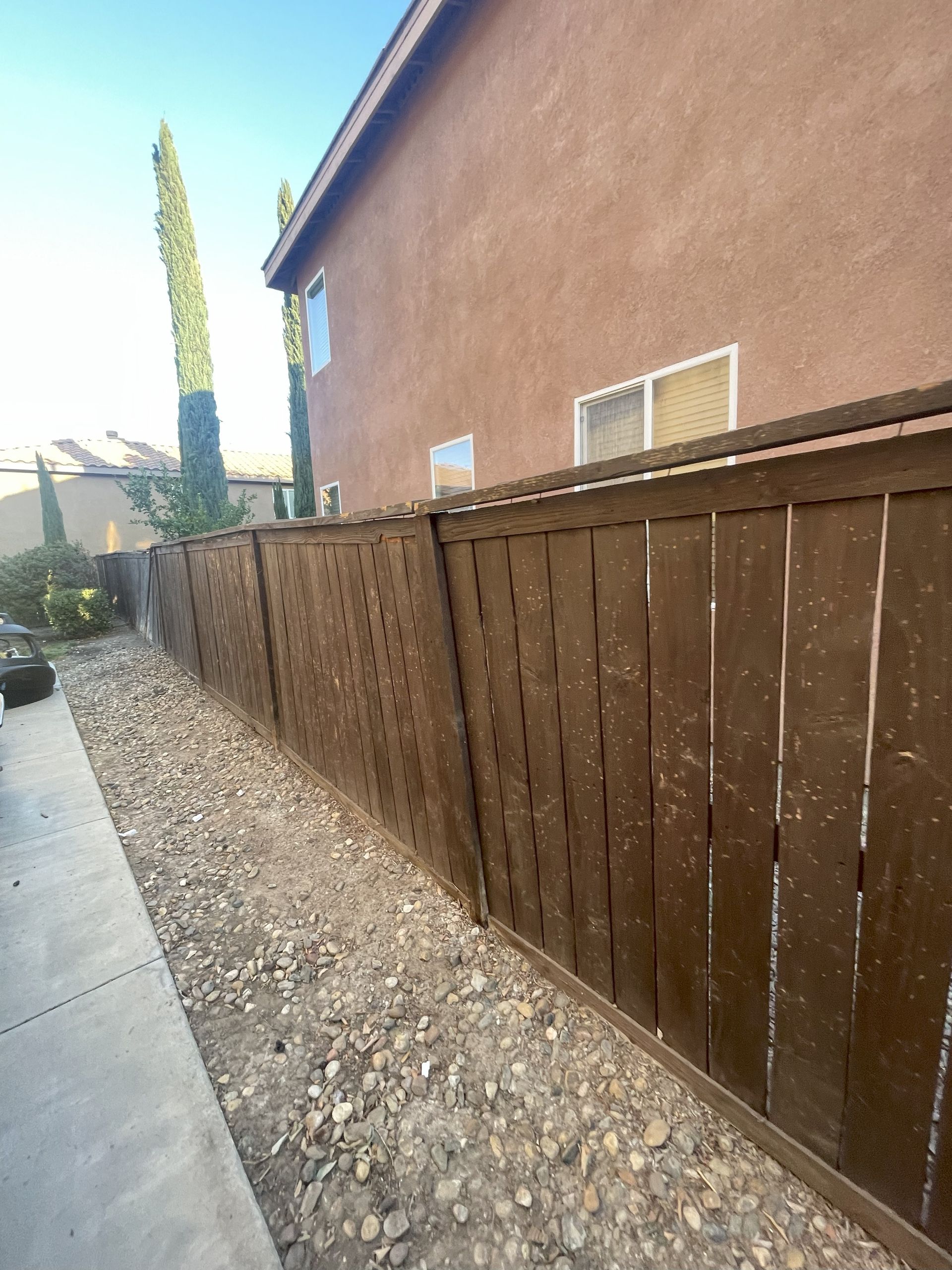 Brown wooden fence next to a gravel-filled yard, beside a stucco house.