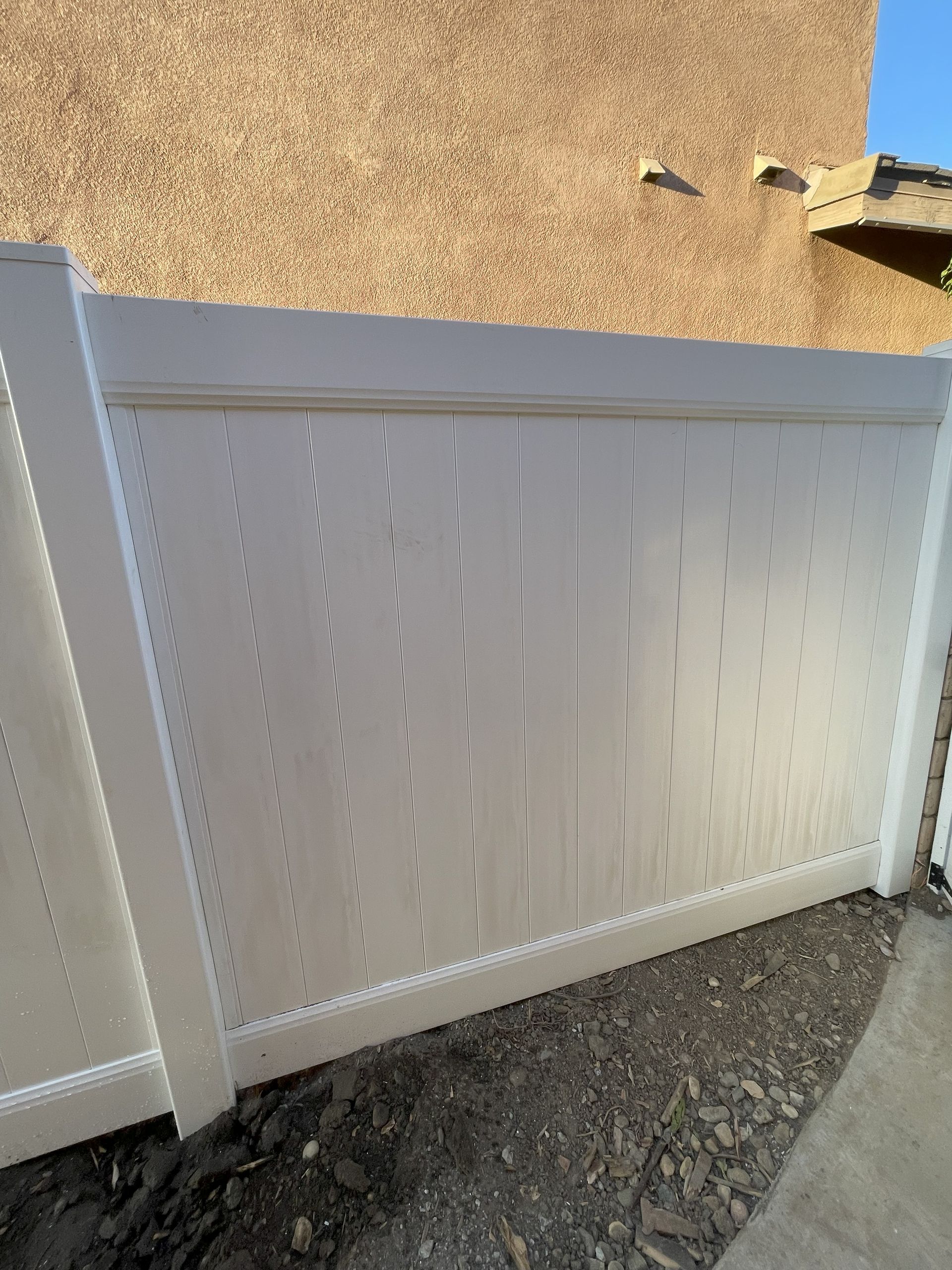 White vinyl privacy fence against a textured beige wall.
