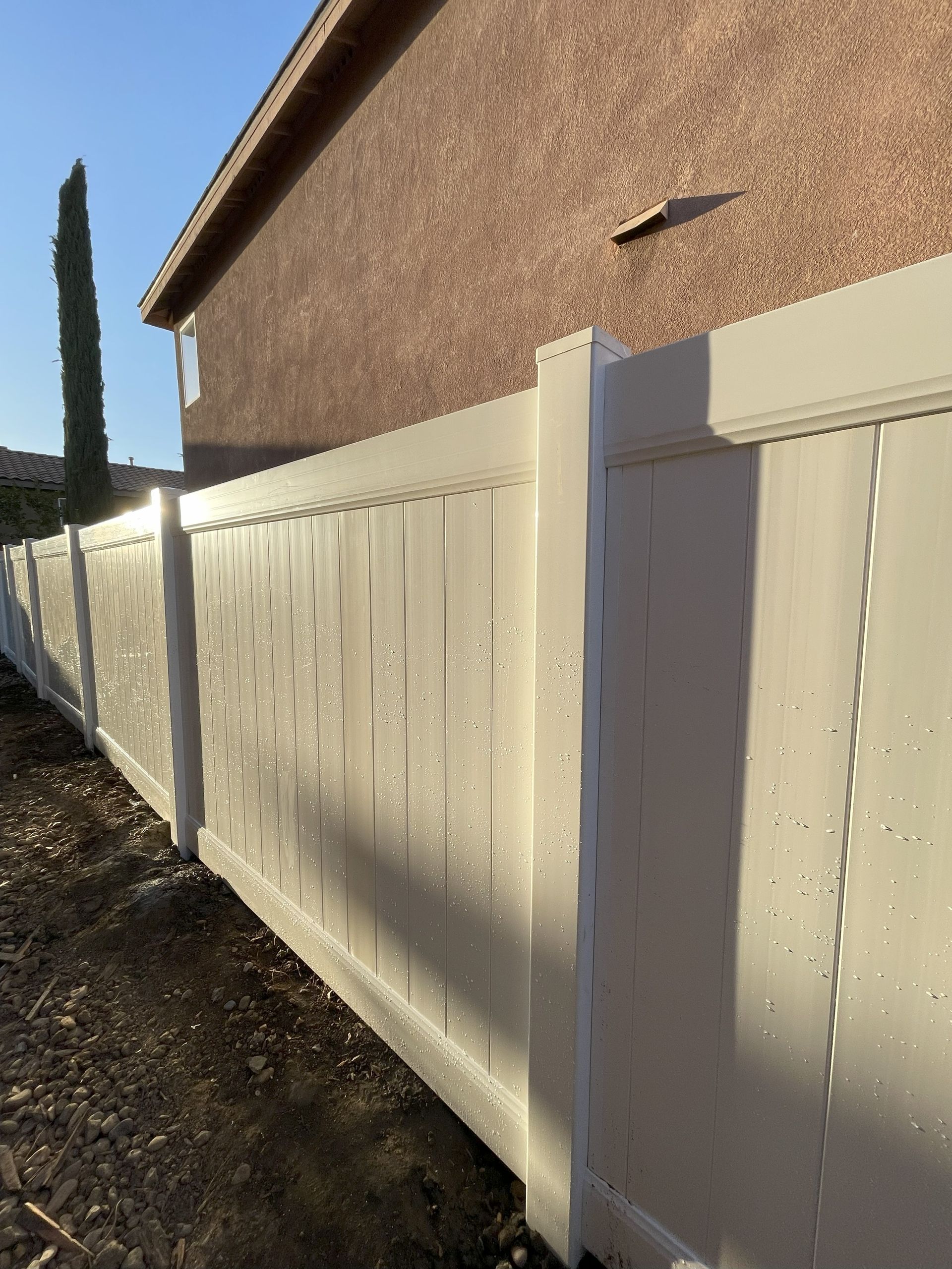 White vinyl fence next to a brown stucco building on a sunny day.