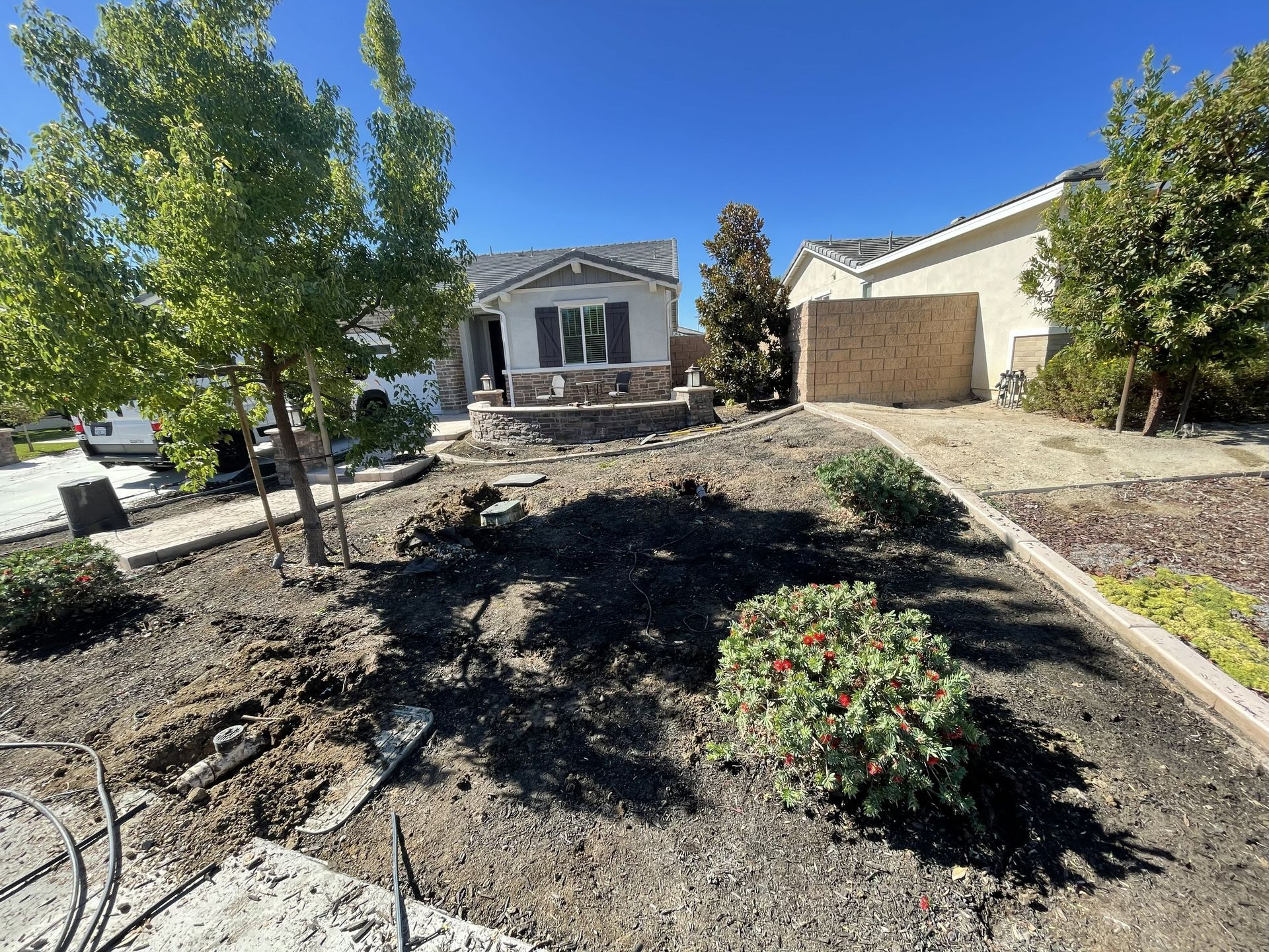 A house with front yard under construction; soil, plants, trees, and blue sky.