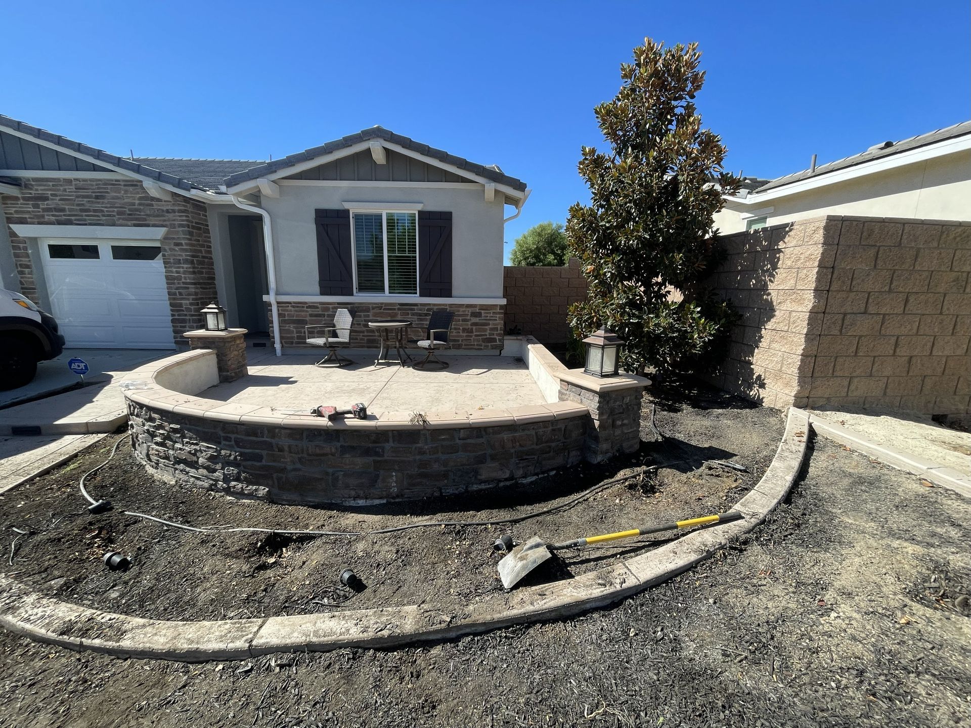 Front yard with newly constructed curved brick wall patio, small tree, and house.