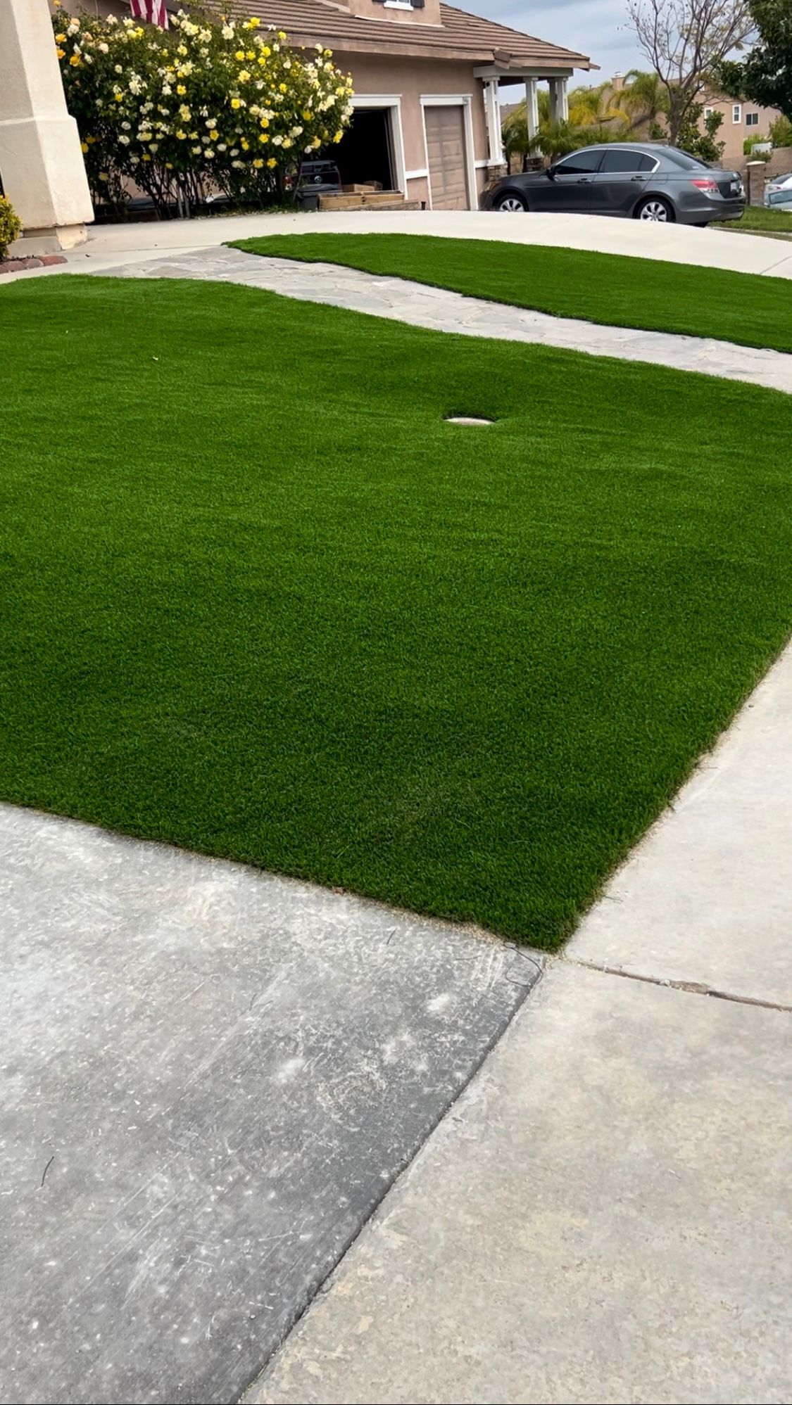 A lawn with a car parked in the driveway and a house in the background.