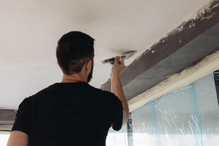 A man is painting a ceiling with a spatula.