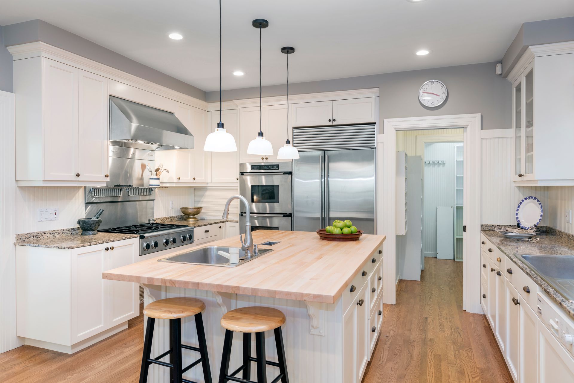 a kitchen with white cabinets , wooden counter tops , stainless steel appliances and a large island .