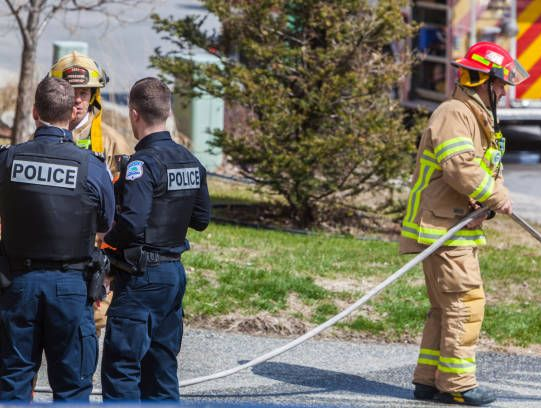 Firefighters in orange suits extinguish a large fire with a water hose.
