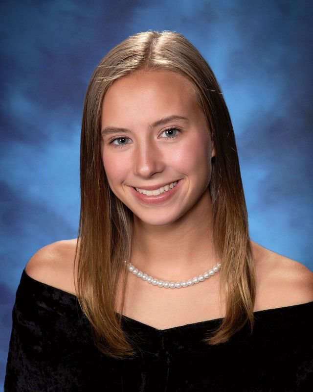 A young woman wearing a pearl necklace is smiling for the camera.