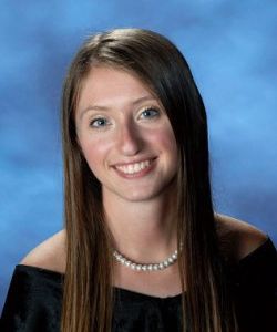 A young woman with long hair and a pearl necklace is smiling for the camera.