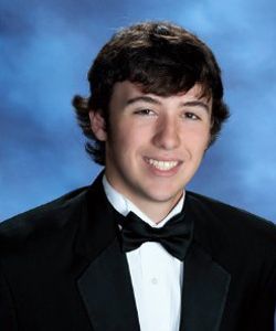 A young man in a tuxedo and bow tie is smiling for the camera.