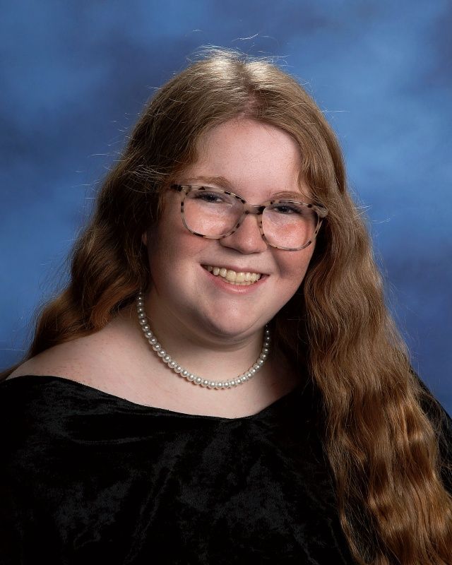 A woman wearing a pearl necklace and a black top is smiling for the camera.