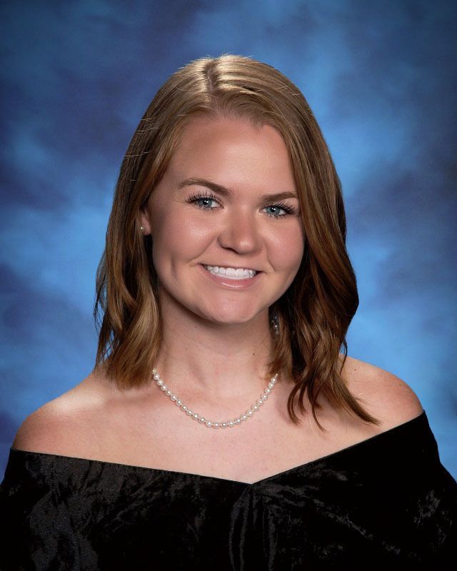 A woman wearing a black off the shoulder top and a pearl necklace is smiling for the camera.