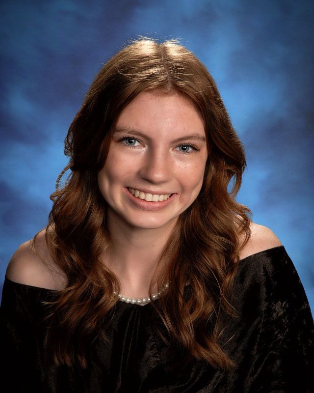 A young woman with long red hair is smiling for a picture.