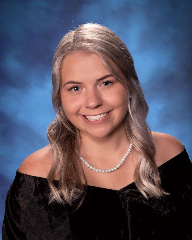 A young woman wearing a black top and a pearl necklace is smiling for the camera.