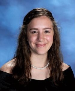 A young woman wearing a black dress and a pearl necklace is smiling for a picture.