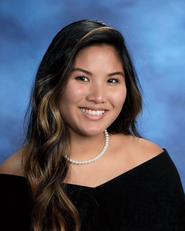 A young woman wearing glasses and a pearl necklace is smiling for the camera.