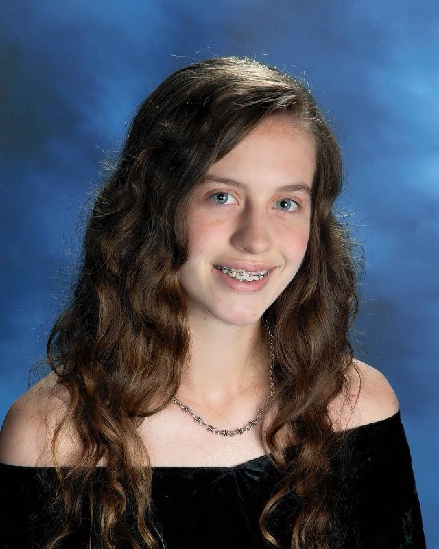 A young woman with long brown hair and a necklace is smiling for a picture.