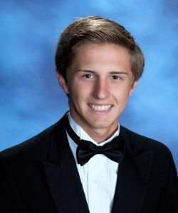 A young man in a tuxedo and bow tie is smiling for a picture.