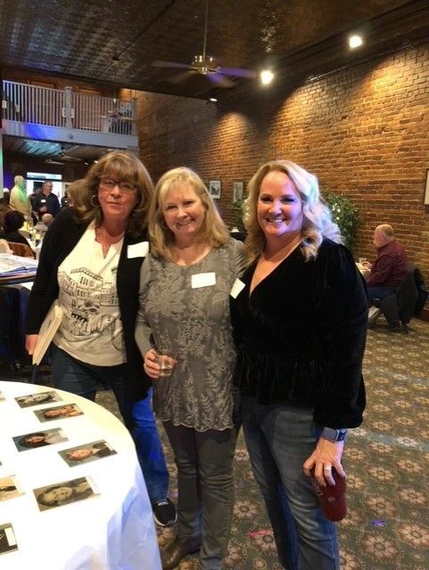 Three women are posing for a picture in a room with a brick wall