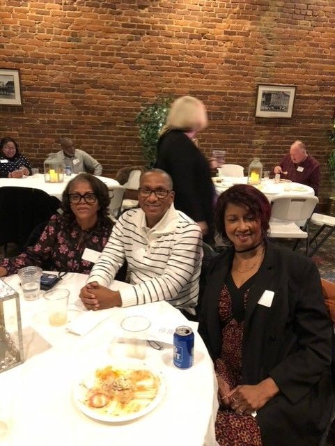 A group of people are sitting at tables in a room with a brick wall.