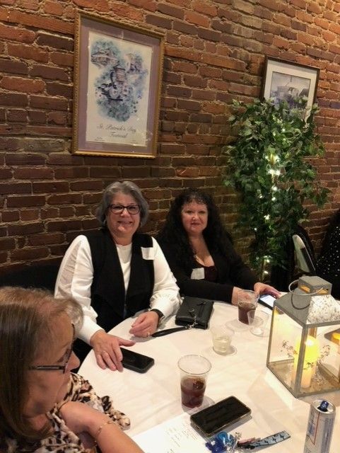 A group of women are sitting at a table in front of a brick wall.