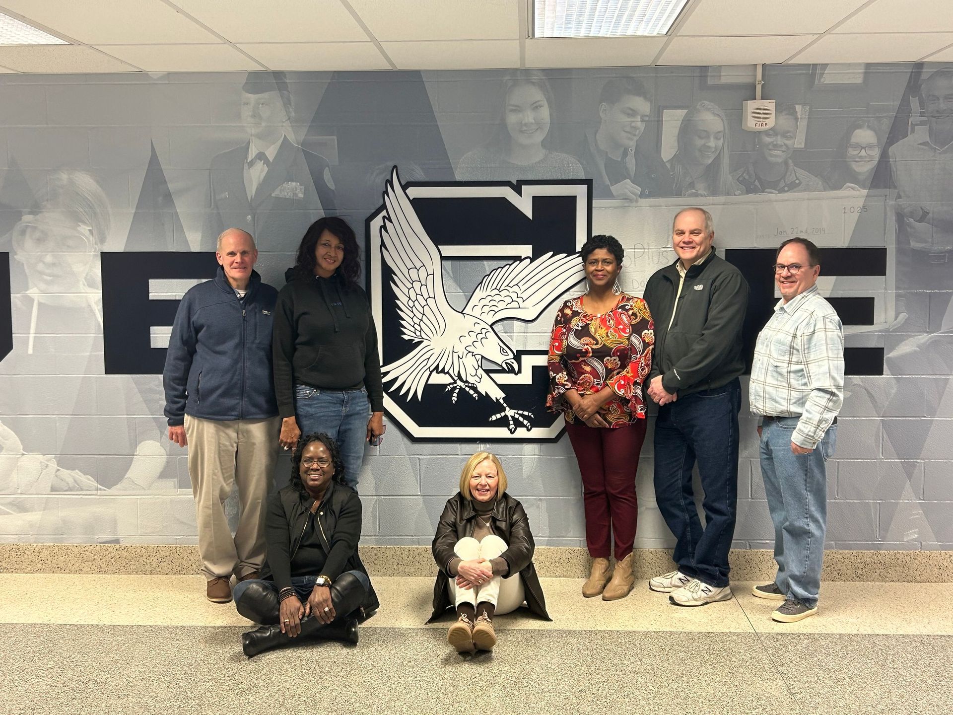 A group of people are posing for a picture in front of a wall with an eagle on it.