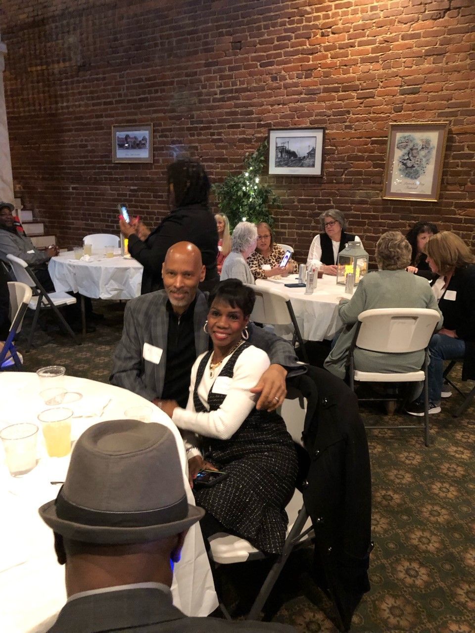 A group of people are sitting at tables in a room with a brick wall.