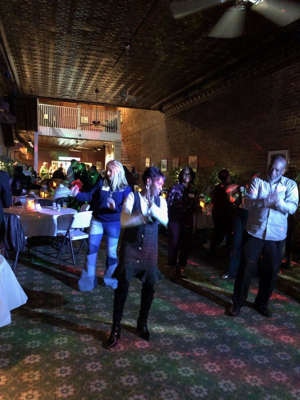 A group of people are dancing in a room with a ceiling fan.