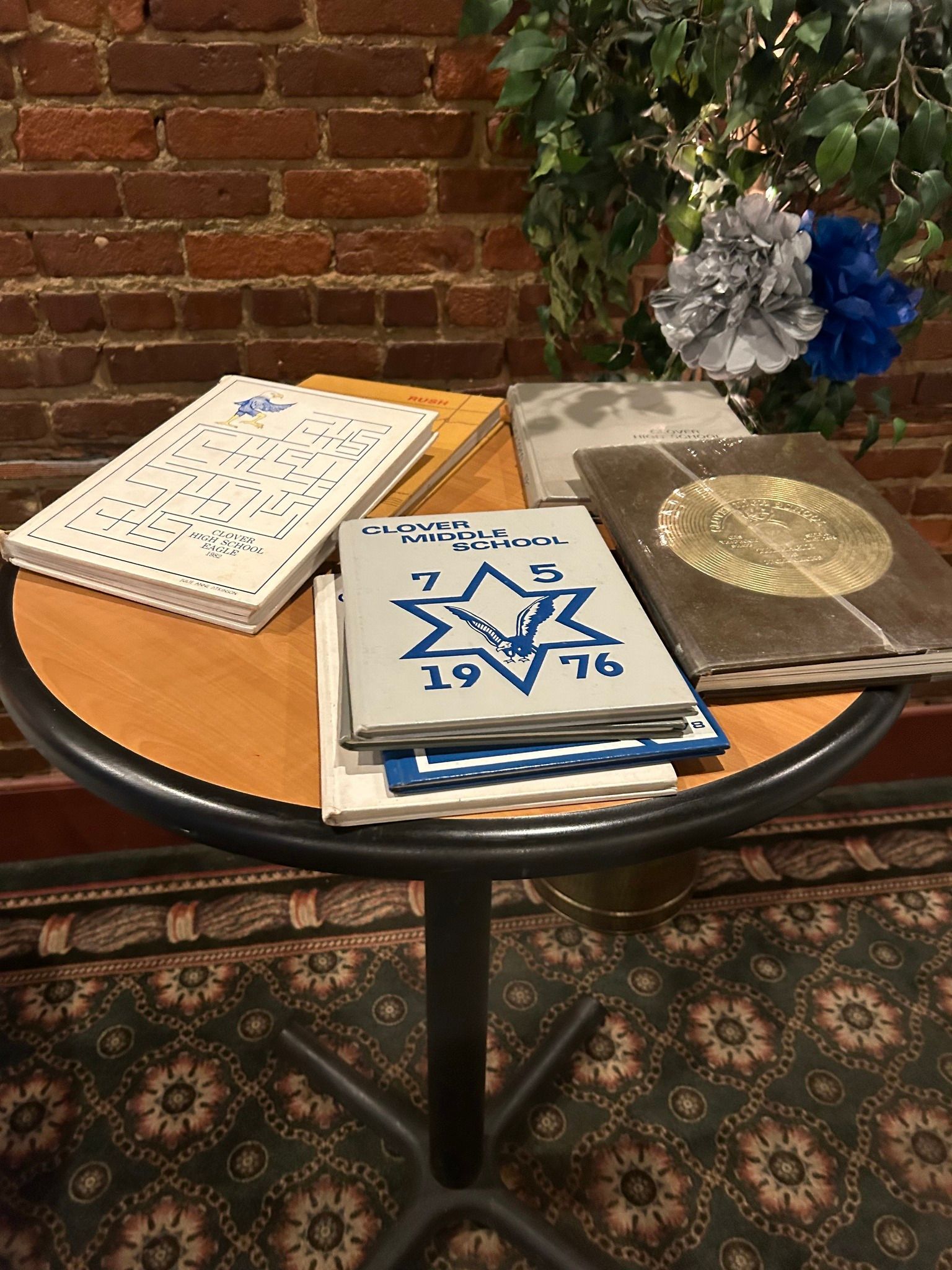 A stack of books on a table with a brick wall in the background.