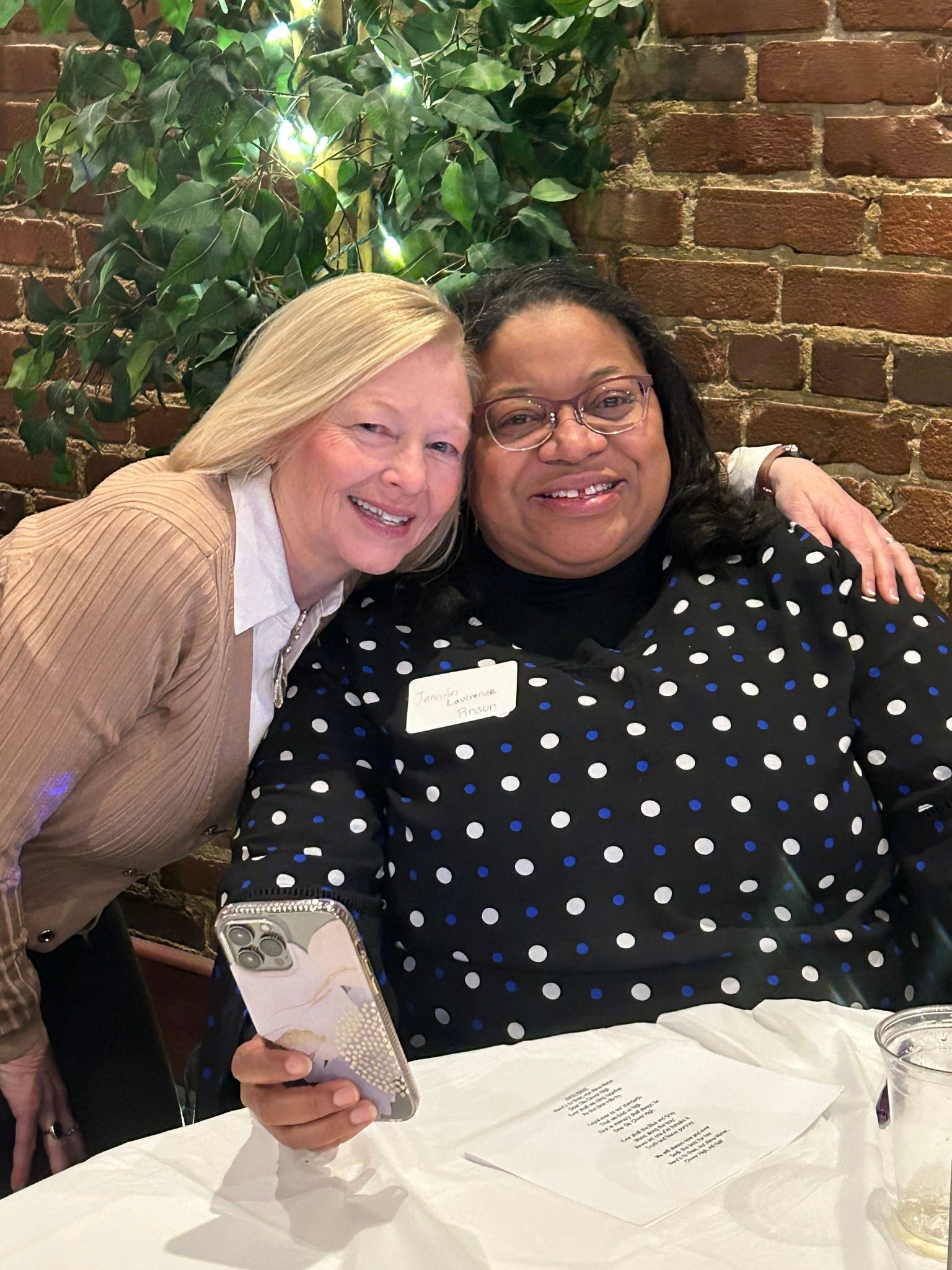 Two women are posing for a picture while sitting at a table.