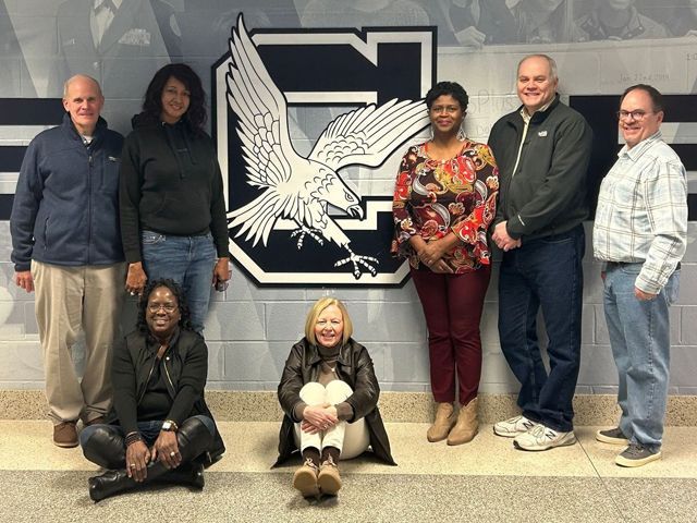 A group of people are posing for a picture in front of a school logo.