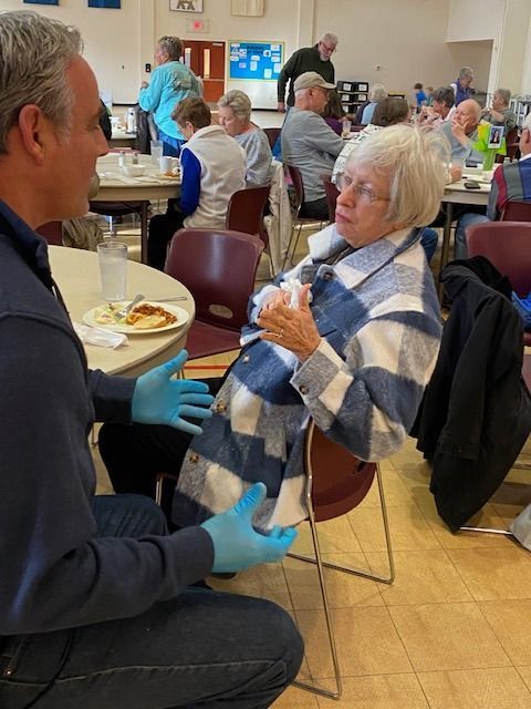 A man wearing blue gloves talks to an older woman