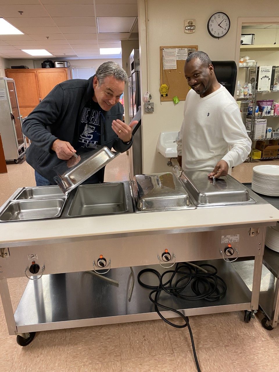 Two men are standing next to a buffet table in a kitchen.