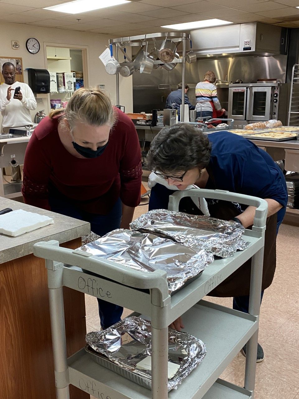 Two women are looking at food on a cart in a kitchen.