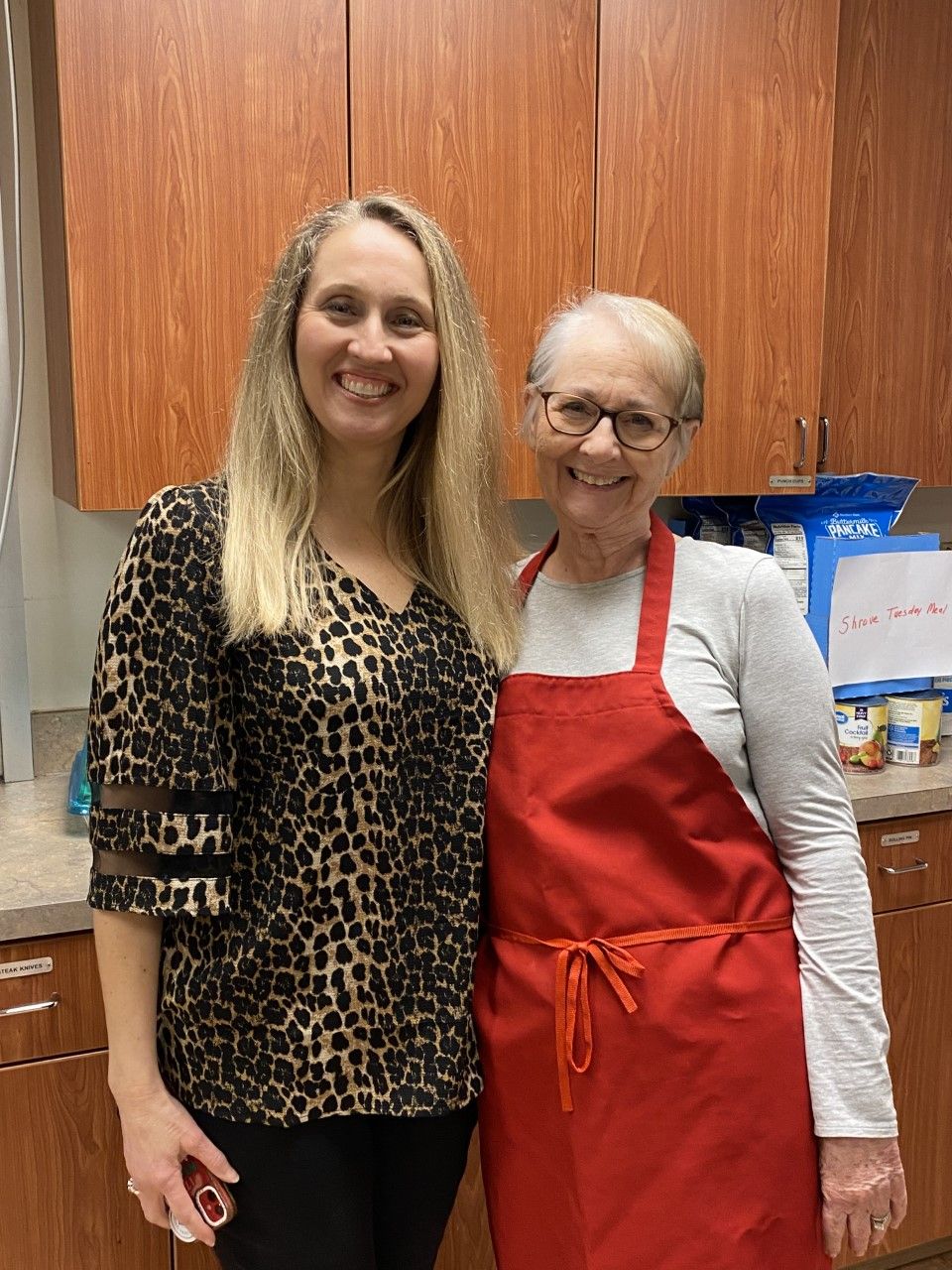 Two women in red aprons are posing for a picture in a kitchen.