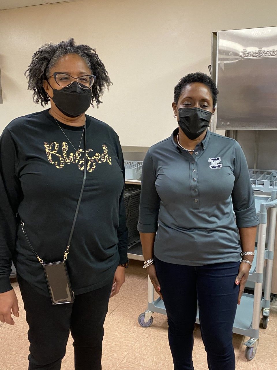 Two women wearing masks are standing next to each other in a kitchen.