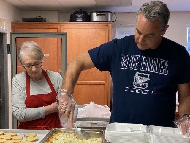 A man wearing a blue eagles shirt is preparing food in a kitchen