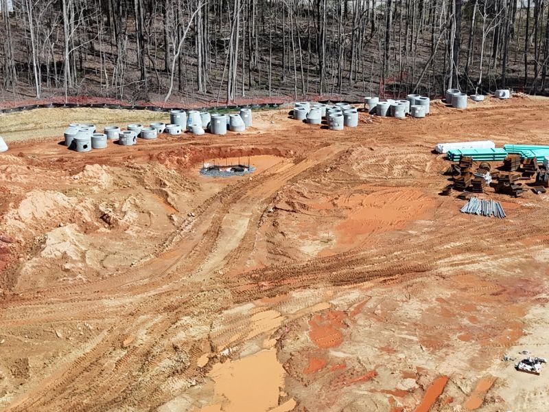 An aerial view of a construction site with a lot of dirt and trees in the background.