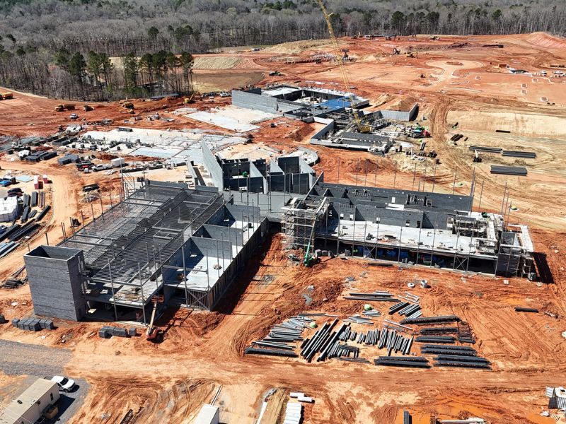 An aerial view of a large building under construction in the middle of a dirt field.