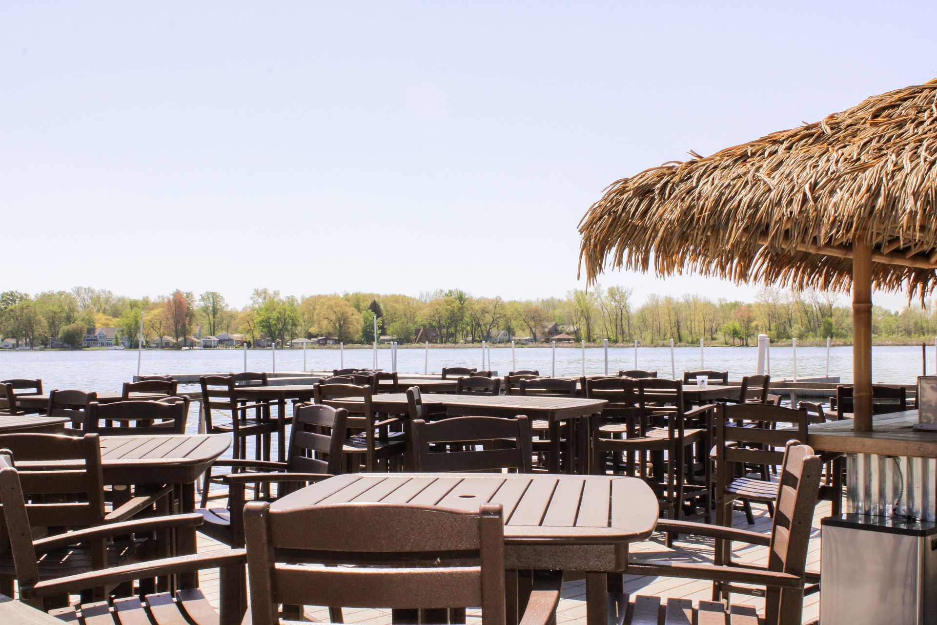 Tables and chairs under a thatched umbrella overlooking a lake