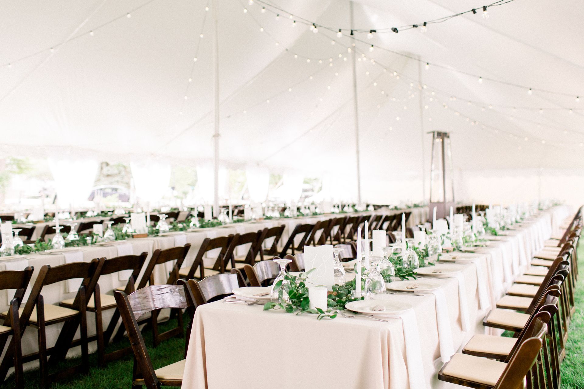 A long table and chairs under a tent for a wedding reception.