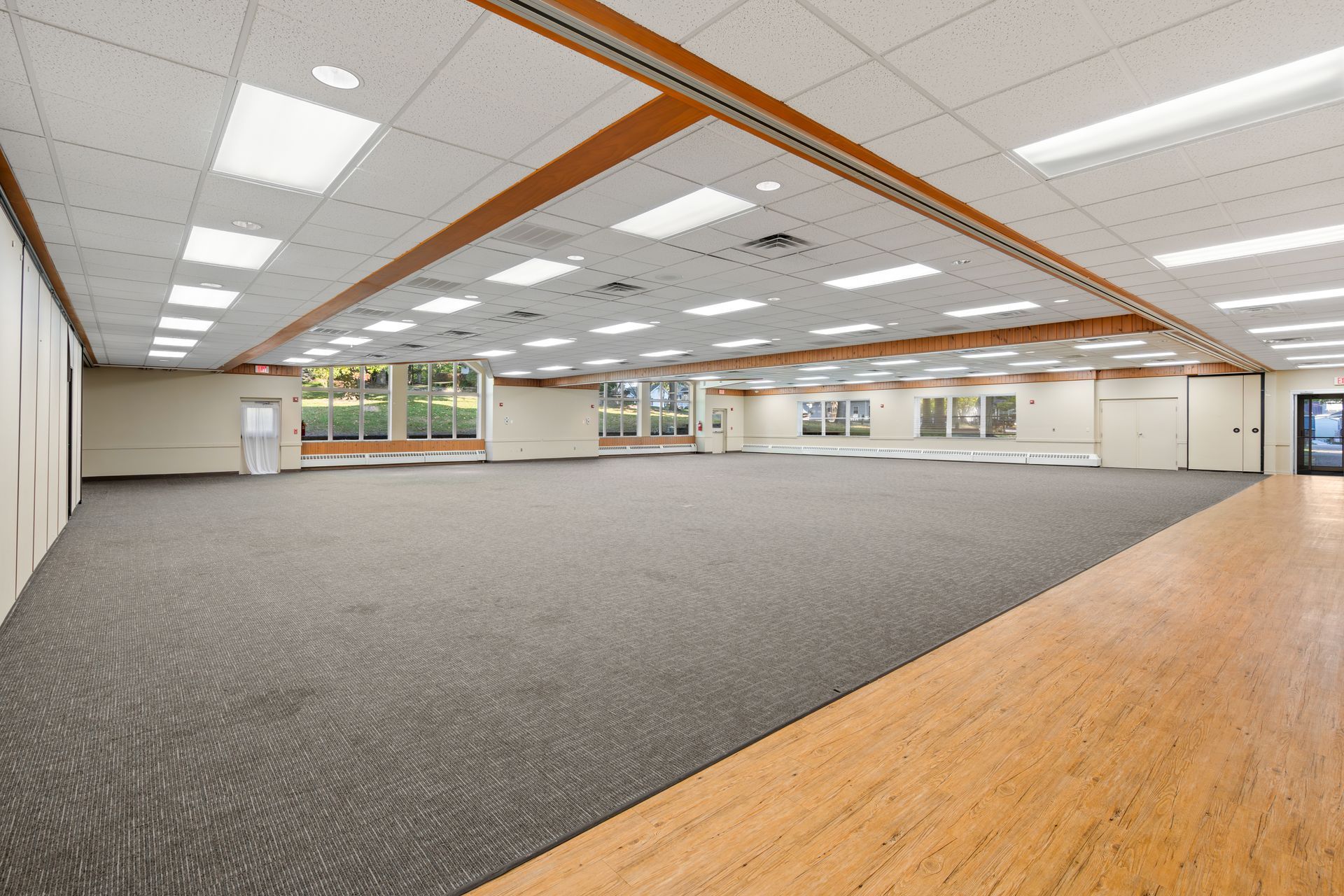 A large empty room with a wooden floor and a carpeted floor.