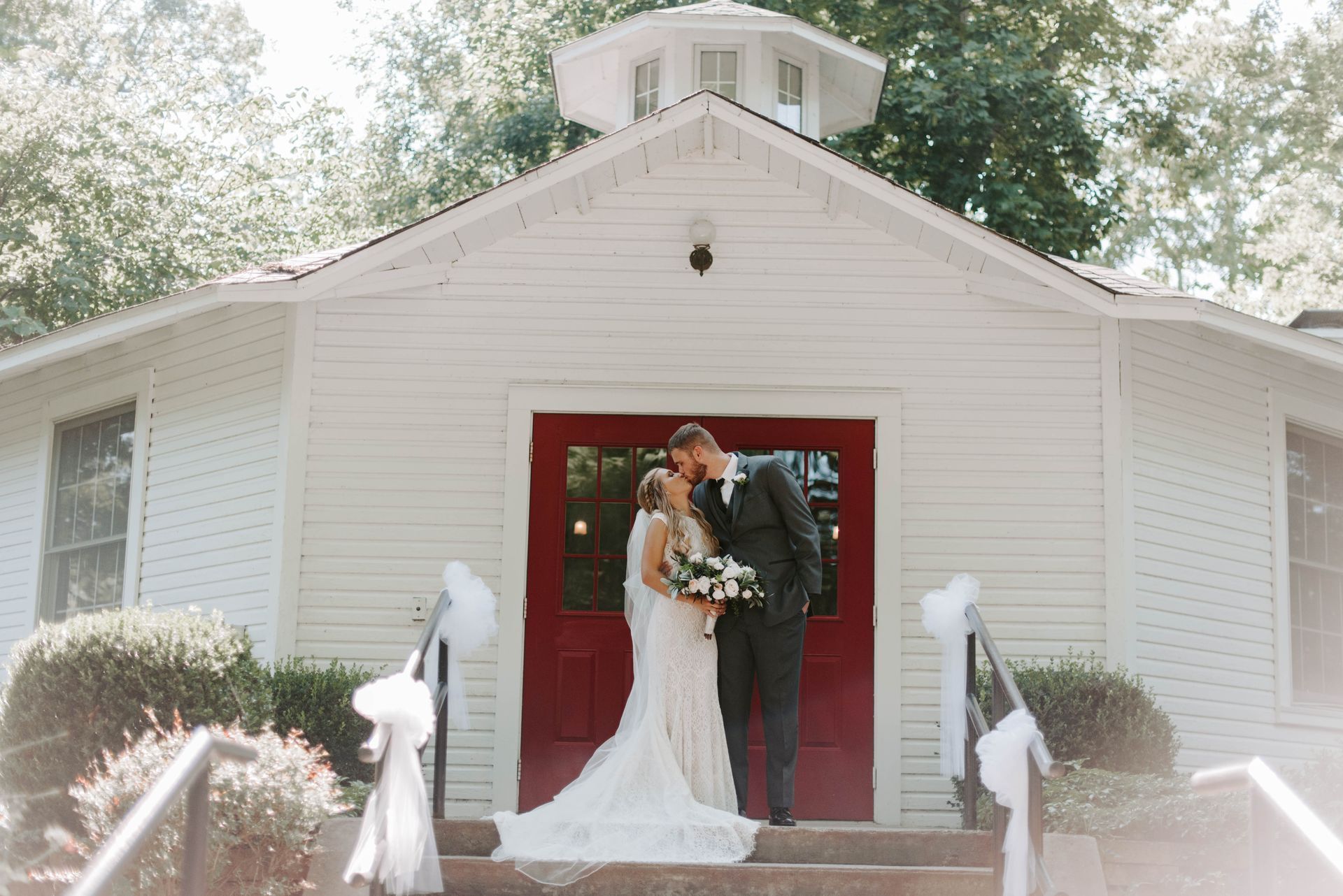 A bride and groom are kissing in front of a white church.