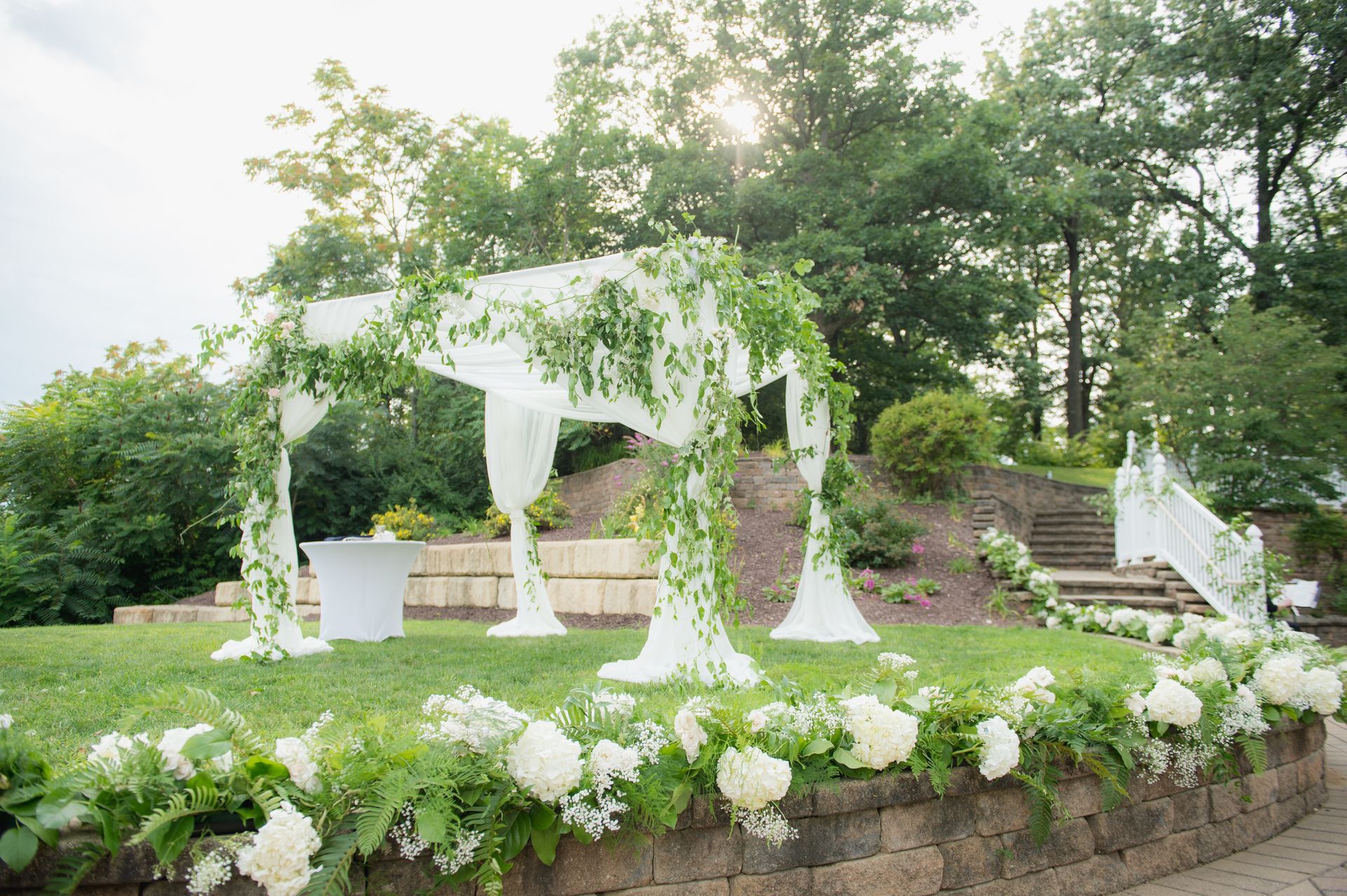A wedding ceremony is taking place in a park with a canopy and flowers.
