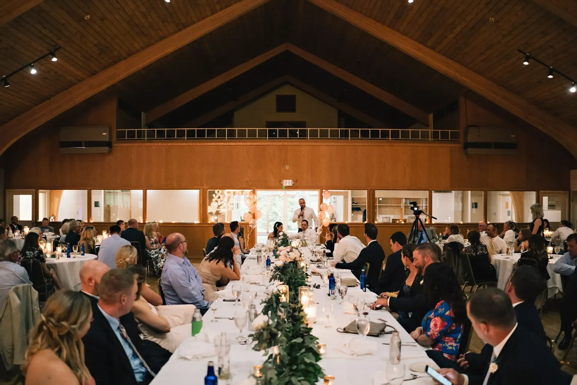 A large group of people are sitting at long tables at a wedding reception.